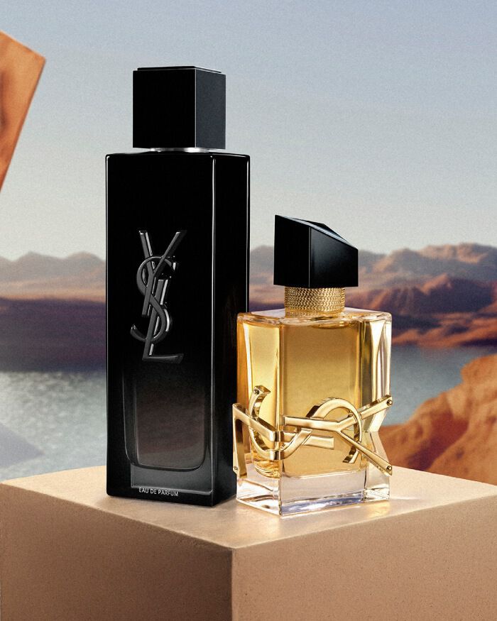 YSL MYSLF EDP 100ml and LIBRE EDP 50ml bottles on a beige pedestal, set against a desert and water landscape.