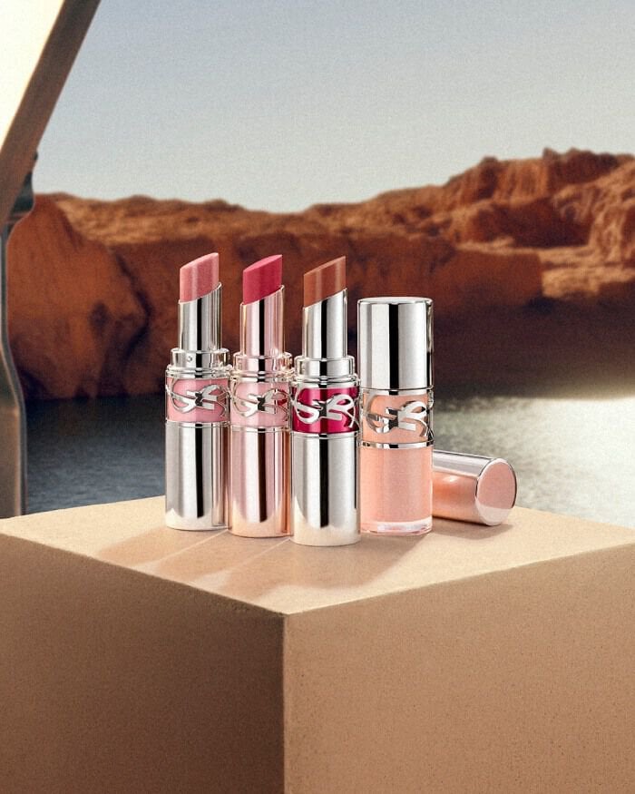 YSL LOVESHINE lipsticks and glosses in shades 19, 11B, and 10 on a beige pedestal in a serene desert landscape.