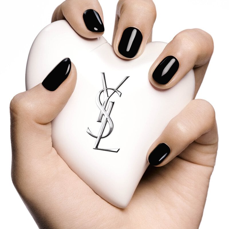 Hand with black nails holding Care Crush Hand & Body serum-in-cream, a white heart-shaped.
