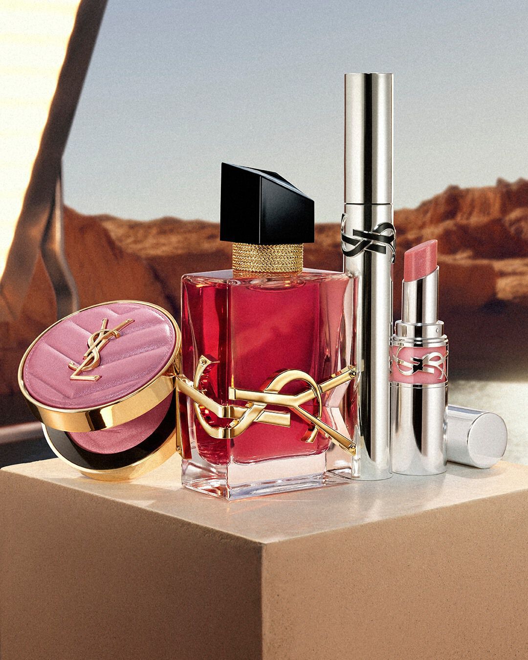 Dua Lipa, YSL Beauty ambassador, with flowing dark hair and a subtle tattoo, gazes directly at the camera in a desert setting.