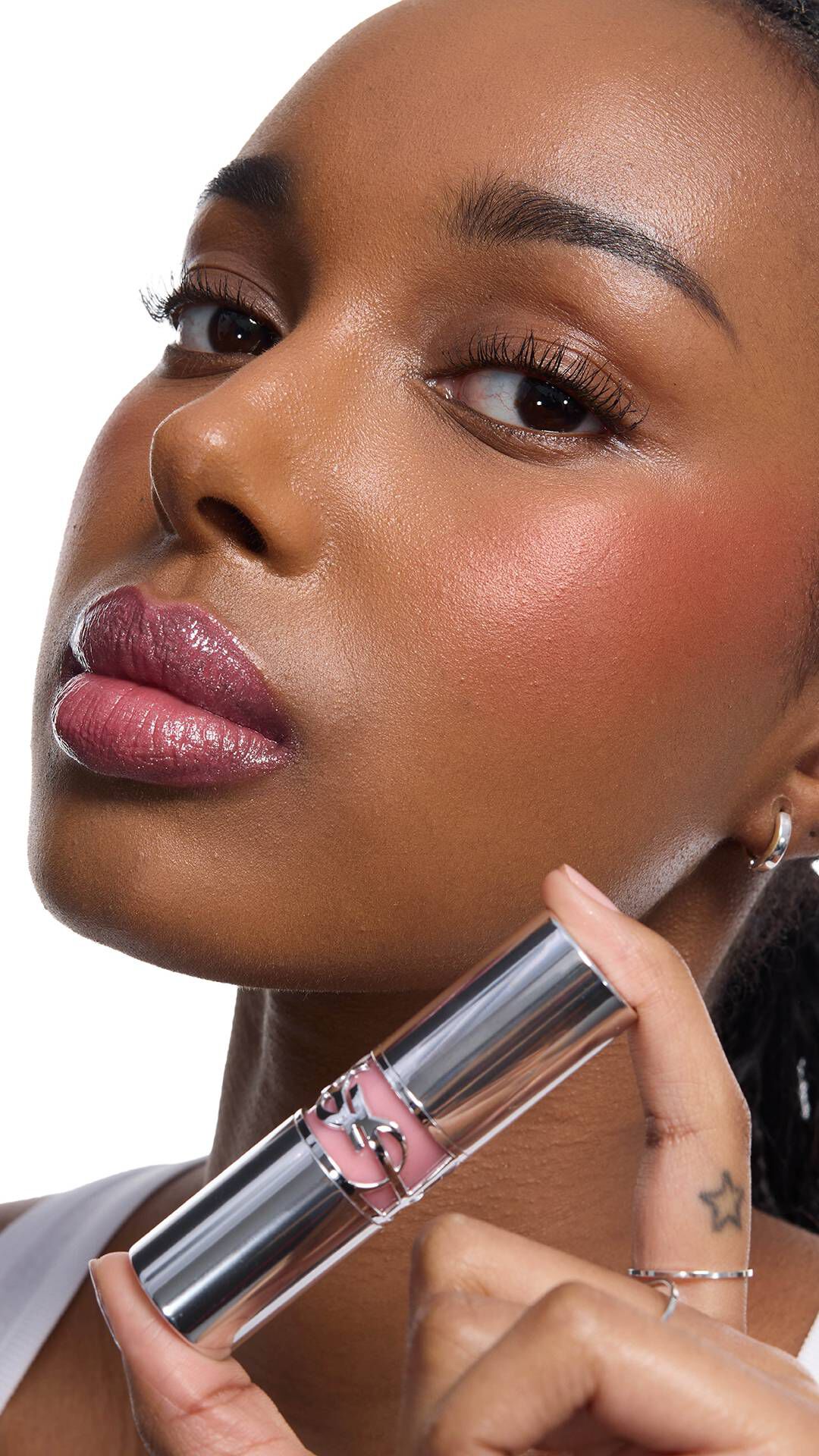 Najma, medium skin, holds YSL LOVESHINE Lipstick. Her lips are
glossy, cheeks show blush.