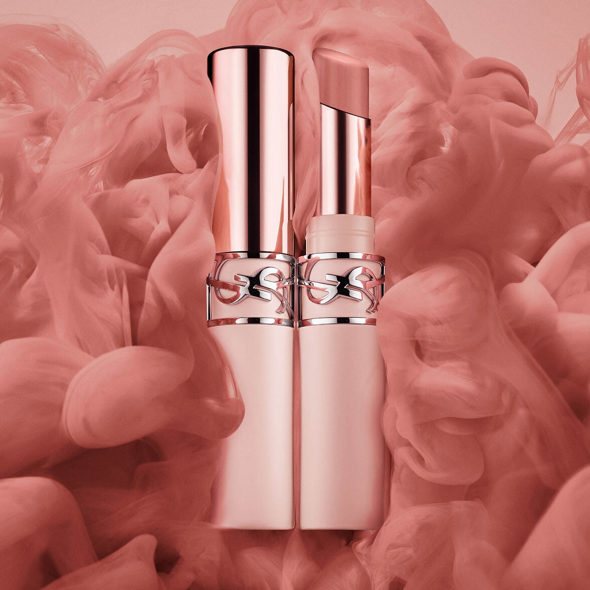 Two YSL LOVENUDE Lip Blusher in Shade 44, one open, one closed, surrounded by pink smoke.